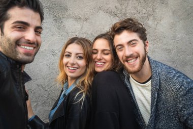 Kameraya gülümseyen bin yılın portresi. Bir grup genç, beton bir duvarın önünde birlikte eğleniyor..