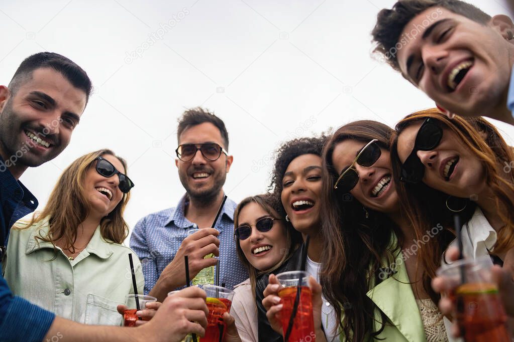 Portrait of young people drinking soft drink cocktails in plastic glasses outdoor and watching the camera.
