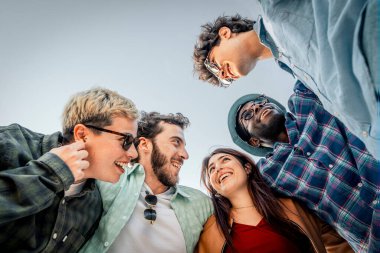 Alçaktan bakıldığında, mutlu bir grup genç arkadaş bir çemberin içinde toplanır ve birbirine güler. Bu, otantik bağlantının ve topluluğun güçlü bir sembolüdür..