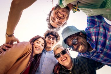 Çevrede toplanmış ve dışarıdaki kameraya gülümseyen mutlu bir grup genç arkadaşın düşük açılı bakış açısı..