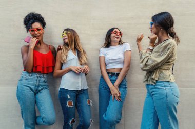 Dört genç bayan arkadaştan oluşan mutlu bir grup renkli gözlük takıyor ve birlikte bir şehir duvarına gülüyorlar..