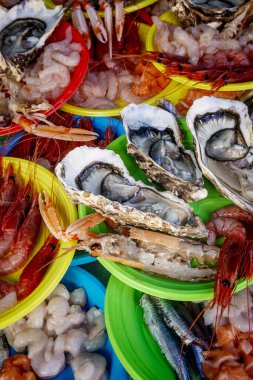 Istakoz, karides ve langoustines de dahil olmak üzere canlı, yakın planda taze çiğ deniz ürünleri bir sokak pazarında renkli plastik tabaklarda servis edilir..