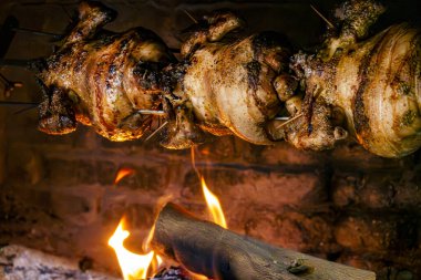 Kavrulmuş tavukların yakın plan çekimi geleneksel tuğla fırınında açık ahşap bir şöminenin üzerine tükürüyor..