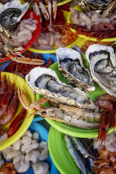 Istakoz, karides ve langoustines de dahil olmak üzere canlı, yakın planda taze çiğ deniz ürünleri bir sokak pazarında renkli plastik tabaklarda servis edilir..