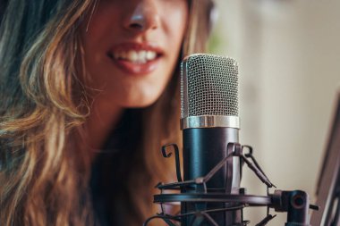 Stüdyo mikrofonuna konuşan bir kadının, podcast, yayın ve ses üzerine uygun bir ses kaydı yapması..