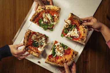 Dört elle, ahşap masadaki pizza kutusundan fesleğen ve domates soslu peynirli pizza dilimleri alırken tepeden tırnağa..