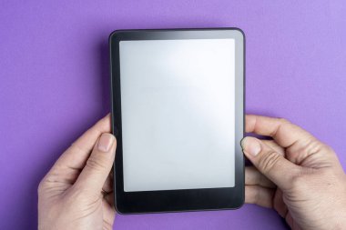 Erkek eller, açık ekran e-okuyucu tabletini parlak mor bir arka plana karşı tutuyorlar, modern teknoloji temaları için yakın çekim.
