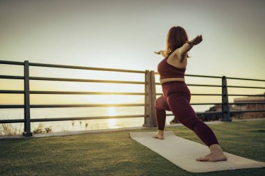 Fit bir kadının minderde yoga hamlesi yapması geniş açıdan görülüyor. Denize yakın denge ve esneklik ve fotokopi alanı olan sporcuların yan görünümü.
