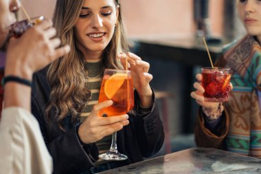 Bir kafede sakin bir sosyal an sırasında elinde spritz kokteyli tutan genç bir kadın. Sıradan bir şehir hayatı ortamında arkadaşlarıyla aperatifin tadını çıkaran bir kadın..