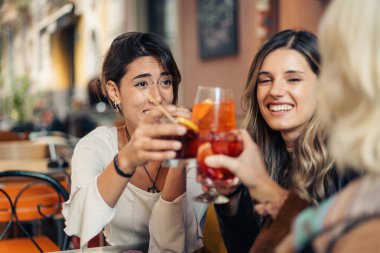 Bir grup arkadaş spritz kokteylleriyle kadeh kaldırıyor. Bir sosyal toplantı sırasında bardakları tokuşturarak bir bar masasında.