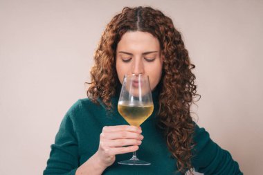 Yeşil balıkçı yaka kazaklı kıvırcık kızıl saçlı genç bir kadın stüdyo tadım oturumunda beyaz şarap kokusu alıyor..