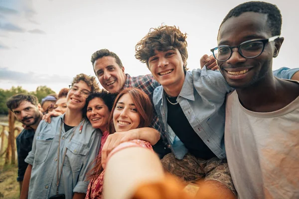Çok kültürlü bir arkadaş grubu açık havada selfie çekiyor. Mutlu genç yetişkinler yaz aylarında arkadaşlığı, çeşitliliği ve topluluğu kutlarken kameraya gülümsüyor..