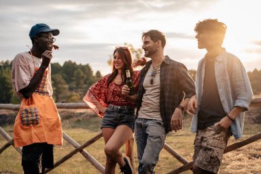 Özgün, genç, çok kültürlü arkadaşlar gün batımında kırsalda takılıyorlar. Özgürlüğü, bağlantıyı, yaz atmosferini ve açık havada rahat sosyal etkileşimi temsil eden doğal kırsal yaşam tarzı..