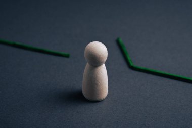 Koyu gri bir yüzeyde, kırık bir yeşil çizginin ortasında duran tek bir tahta bebek insan darboğazını, iş akışı kesintisini ya da bir iş sürecindeki duraklamayı temsil eder..