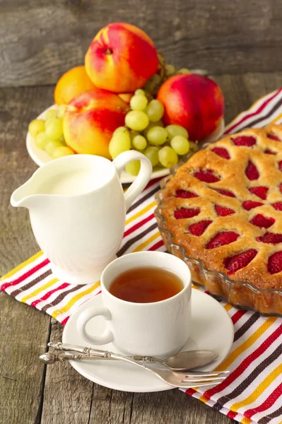 Jordgubbstårta med te, mjölk och frukt till frukost — Stockfoto