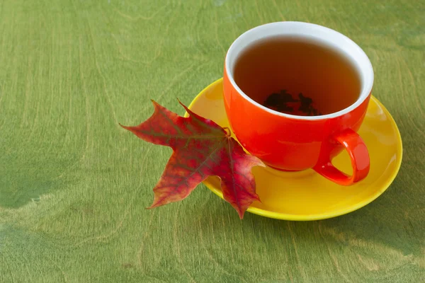 Šálek čaje a na podzim javorový list na zelené dřevěné pozadí — Stock fotografie