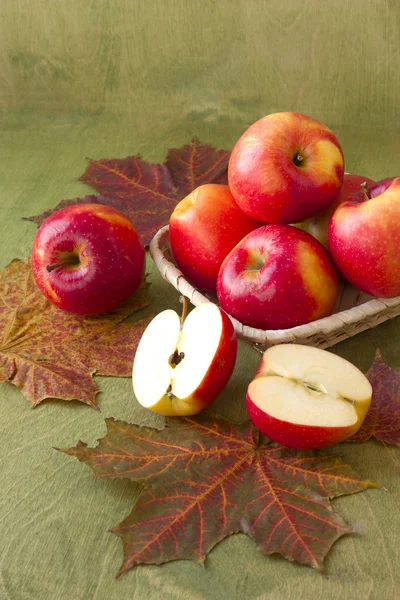 Apples in a basket on a table strewn with autumn leaves — Stock Photo, Image