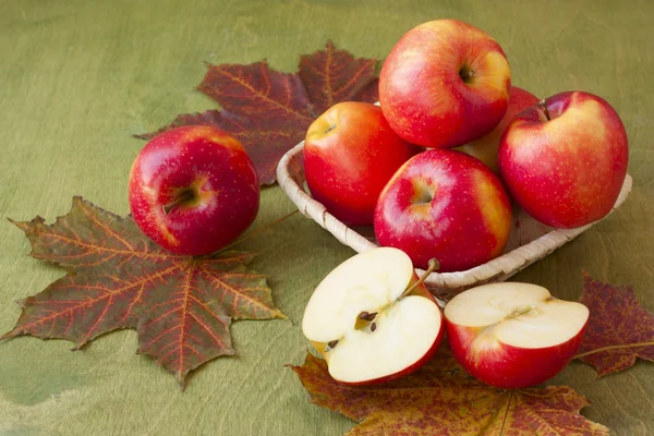 Apples in a basket on a table strewn with autumn leaves — Stock Photo, Image