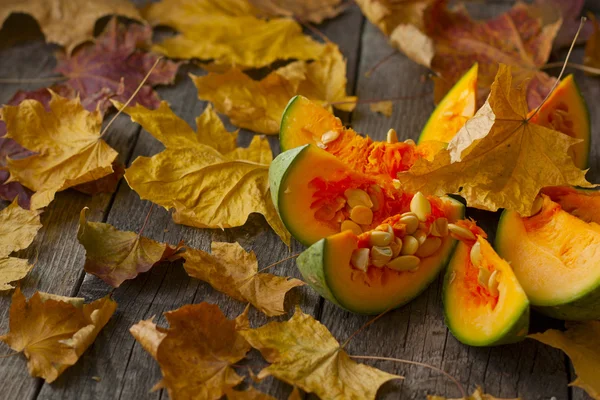 Pumpkin, cut into pieces on a wooden background strewn with autu — Stock Photo, Image