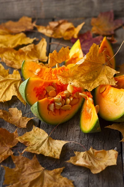 Pumpkin cut into pieces on a wooden background strewn with autum — Stock Photo, Image