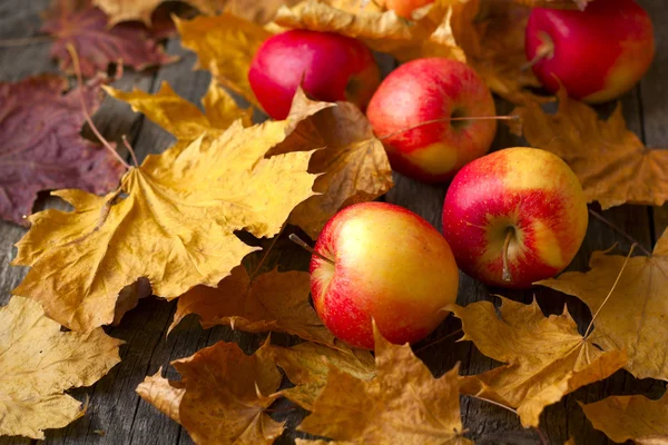 Fresh apples on a table strewn with autumn leaves — Stock Photo, Image