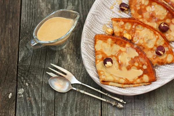 Frittelle su un piatto con salsa di caramello e noci su un dorso di legno — Foto Stock