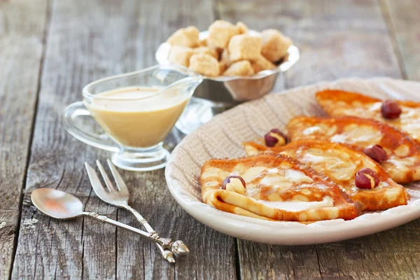 Frittelle su un piatto con salsa al caramello e noci su un bac di legno — Foto Stock