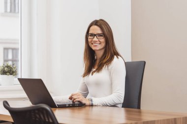 Gülümseyen iş kadını masada oturuyor ve dizüstü bilgisayarla çalışıyor. Ofiste çalış. İş adamları