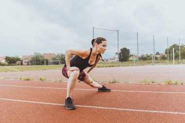 Dişi koşucu, koşan oval alanda ısınıyor. Esniyorum.