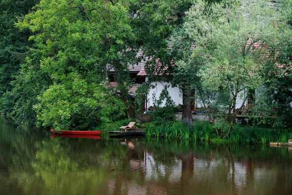 Un lugar tranquilo en el agua con un barco rojo, casa de campo y árboles en —  Fotos de Stock
