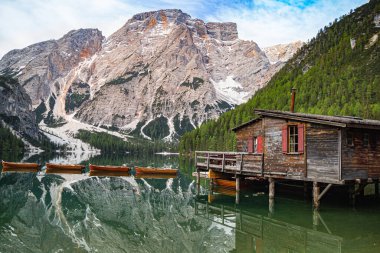 Dolomitler, Unesco Dünya Mirası, Güney Tyrol, İtalya 'daki Pragser Wildsee (Lago di Braies) ikonik dağ gölünün berrak sularında yansıyan kayıkhane ve Seekofel Dağı' nın alçak açılı görüntüsü