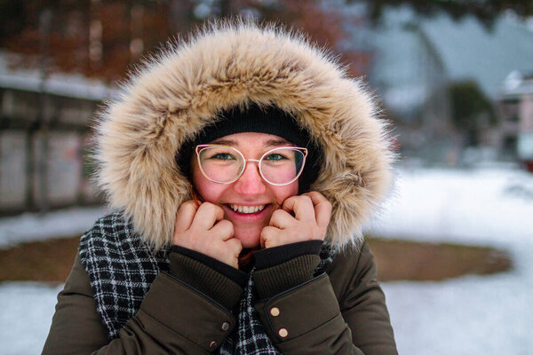 Happy young woman smiling and protecting her hand against the cold under a furry jacket in winter as she has forgotten to wear gloves