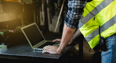 Bir fabrika mühendisi, üretimi kontrol etmek ve bir metal fabrikasındaki mekanikleri bulmak için bir masa üzerinde çalışmak için dizüstü bilgisayar kullanır..