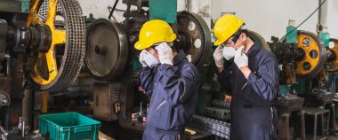 Üniformalı fabrika tamircileri metal fabrikasında çalışmadan önce yüz maskesi takıyorlar..