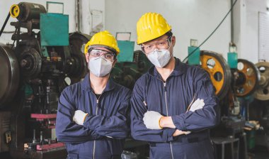 Üniformalarıyla maske takan endüstriyel işçiler bir metal fabrikasında kollarını kavuşturdular..