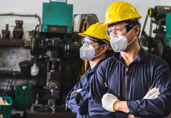 Üniformalarıyla maske takan endüstriyel işçiler bir metal fabrikasında kollarını kavuşturdular..