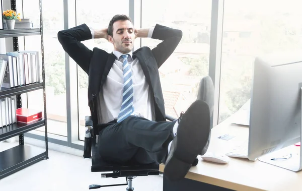 A business manager reclining and put his feet up on computer desk to relaxing in the office.