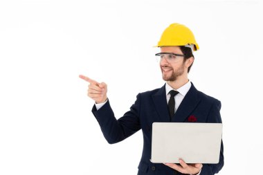 Akıllı genç mimar gözlük takıyor ve planlanan işi kontrol etmek için elinde dizüstü bilgisayar tutan sarı kasklı. Pankart için resim beyazından izole edilmiş arkaplan.