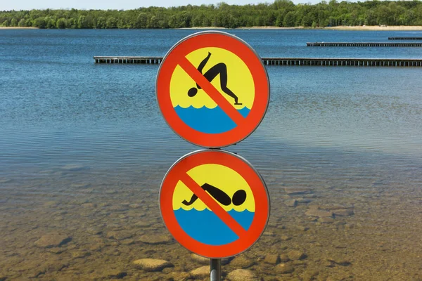 No swimming beach sign. Jumping into water is forbidden. Safety lake shore restrictions. Shallow water danger background.