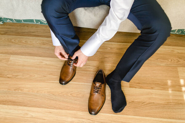 Leather shoe lacing. Businessman in white shirt and suit trousers. Groom getting ready for the wedding. Wearing clothes background.