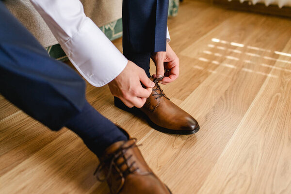 Leather shoe lacing. Businessman in white shirt and suit trousers. Groom getting ready for the wedding. Wearing clothes background.