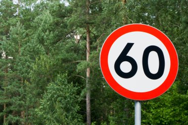 Arkasında ağaçlar olan hız limiti tabelası. Saatte maksimum 60 kilometre. Orman arka planında yol güvenliği. Beyaz yuvarlak kırmızı sınır çizgisi.