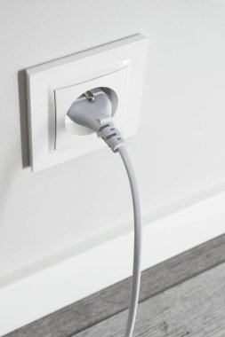 Gri duvarda yepyeni bir priz var. Beyaz kablo fişi takılı. Stüdyonun yenilenmiş elektrik kaynağı geçmişi. Boş kopyalama alanı beyaz plastik güç kaynağı.