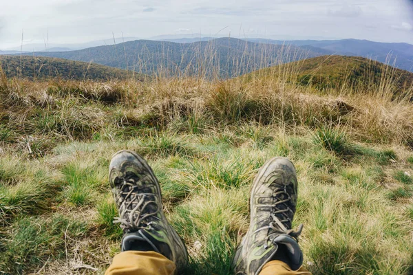 Mountain trekking background. Trekking shoes covered in mud. Bieszczady National Park in Poland. Relax on the top of the hill. Male tourist sitting on autumn meadow ground.