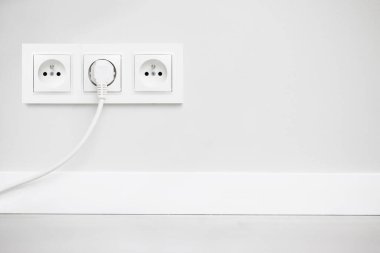 Gri duvarda izole edilmiş elektrik prizi. Beyaz kablo fişi takılı. Stüdyonun yenilenmiş elektrik kaynağı geçmişi. Boş kopyalama alanı çifte beyaz plastik güç kaynağı.