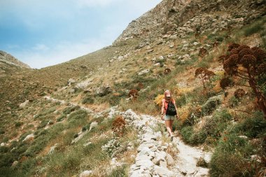 Dağların arkasında sırt çantalı beyaz elbiseli genç bir kadın.