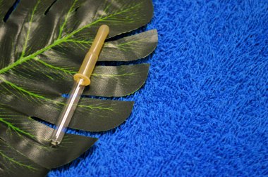 Pipet palmiye yaprağının üzerinde, mavi kumaşın arka planında yatıyor.