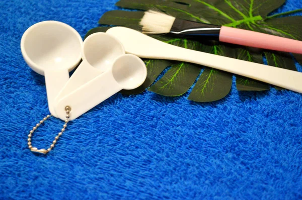 Brush with a spatula for applying masks and measuring spoons lie on palm leaf — Stock Photo, Image