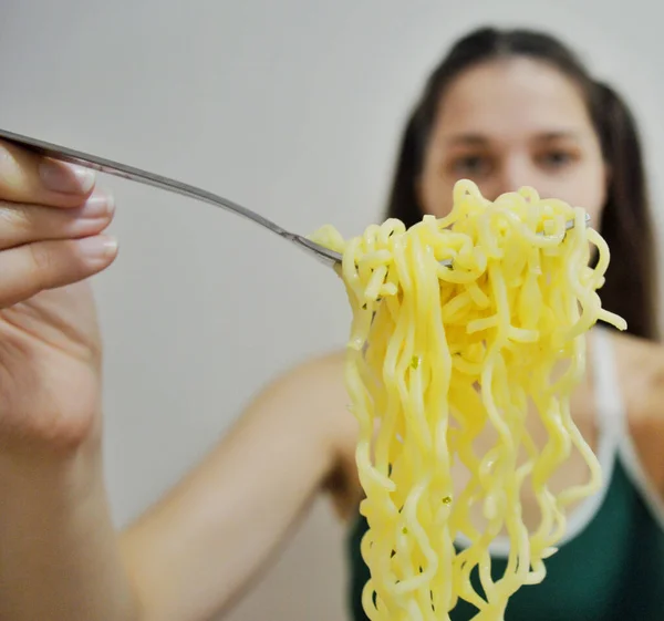 若いです女の子とともに暗いです髪食べるインスタントラーメンとともにフォークで光の背景 — ストック写真