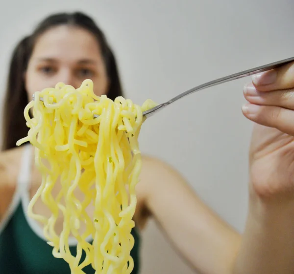 若いです女の子とともに暗いです髪食べるインスタントラーメンとともにフォークで光の背景 — ストック写真